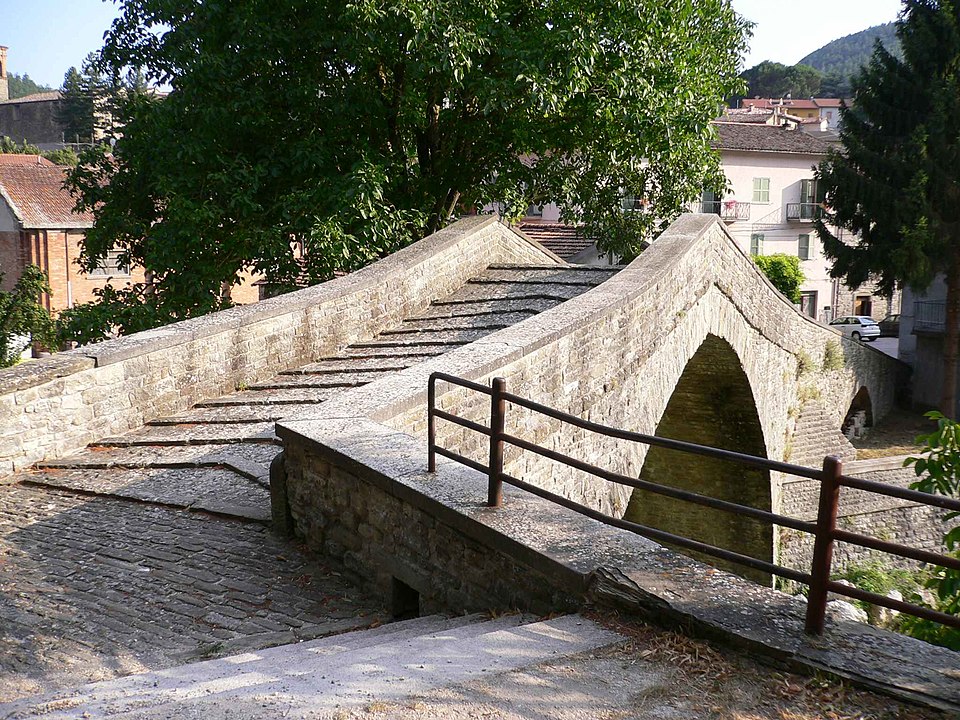 Medieval stone bridge over the Biscubio river in Apecchio with arched spans reflected in the water